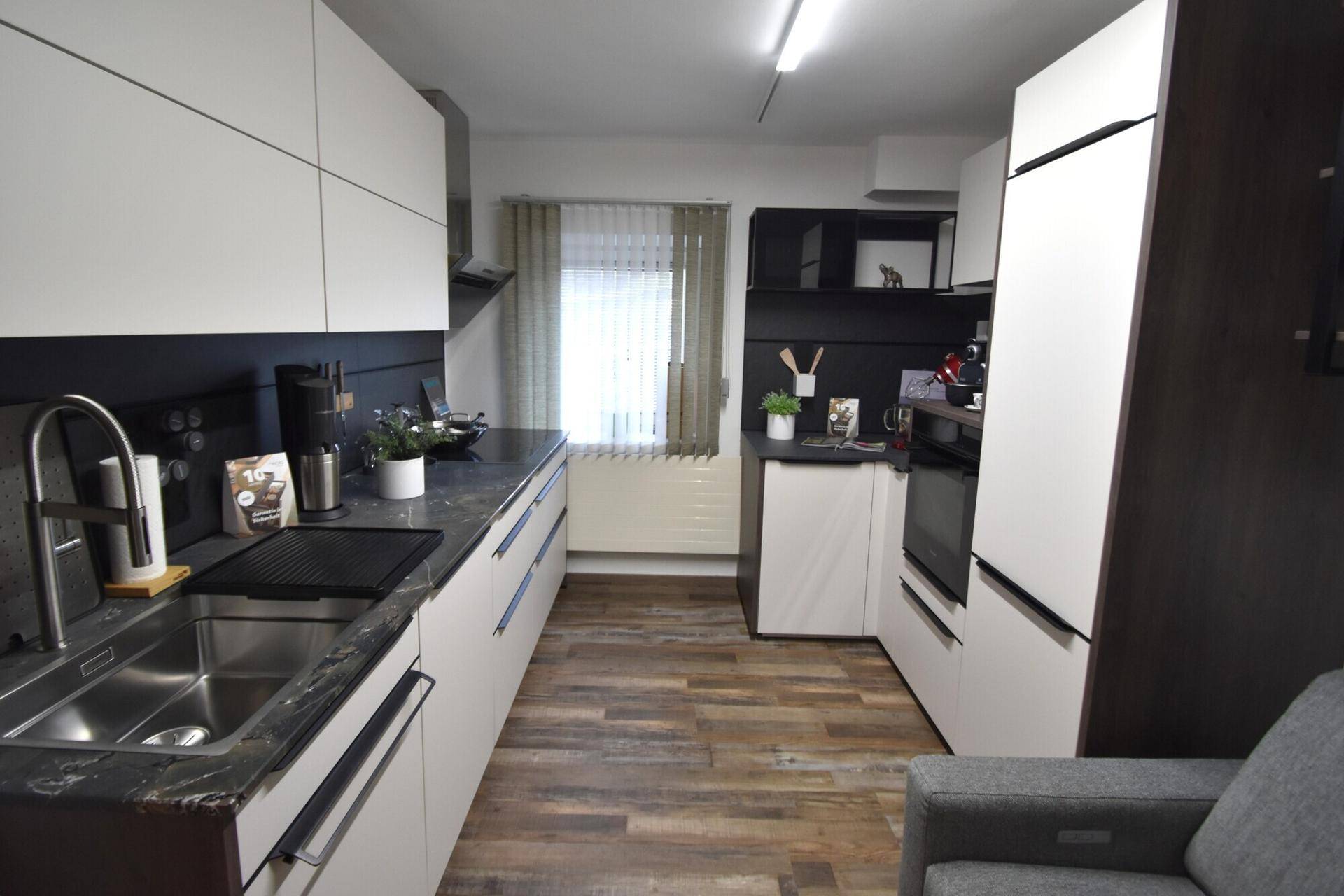 Moderne Einbauküche mit weißen und dunklen Schränken, ausgestattet mit Spüle und Geräten.