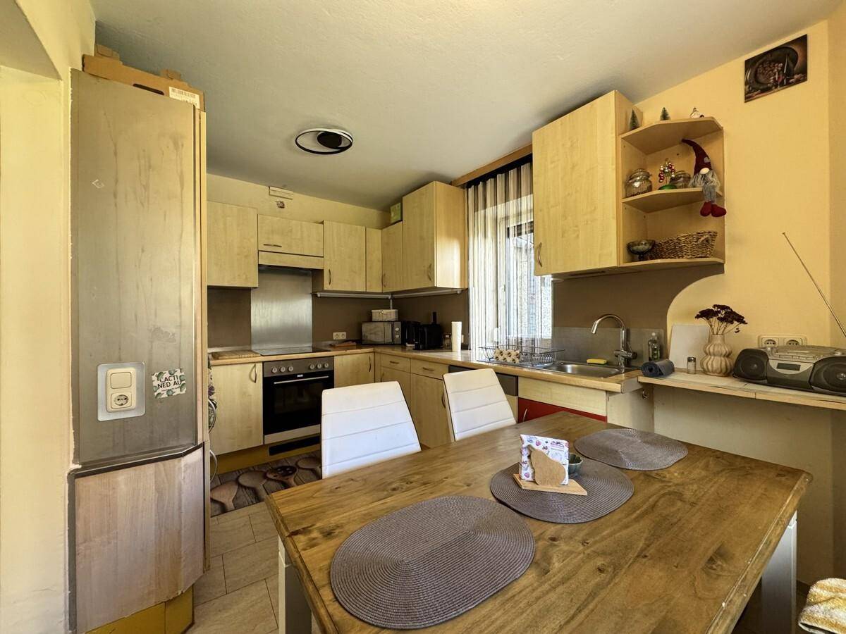 Gemütliche Wohnküche mit Holztisch, hellen Holzschränken und integrierten Geräten.