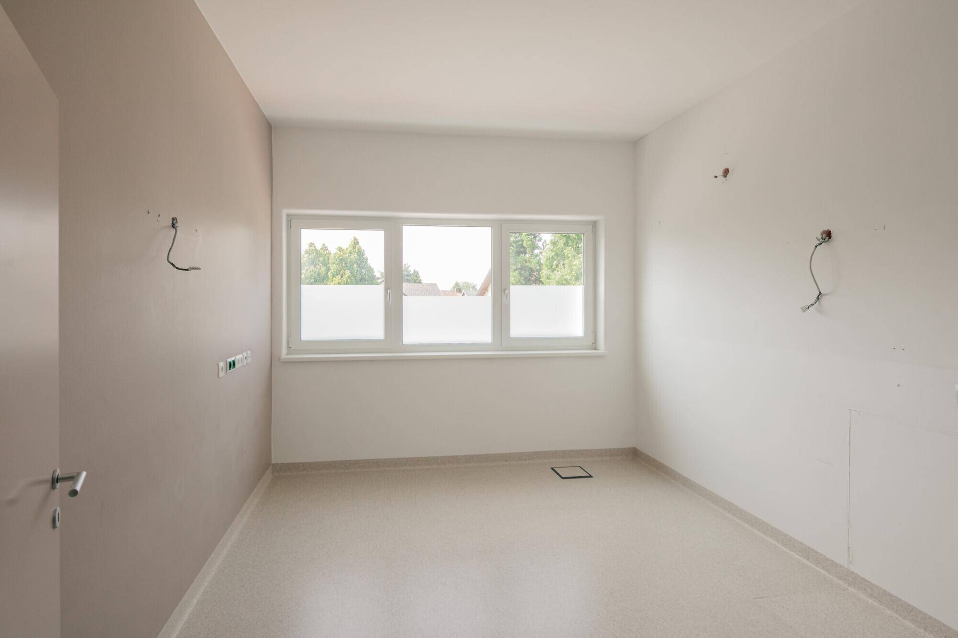 Moderner Büroraum mit hellem Vinylboden und großem Fenster, ideal für flexible Nutzung und Gestaltung.