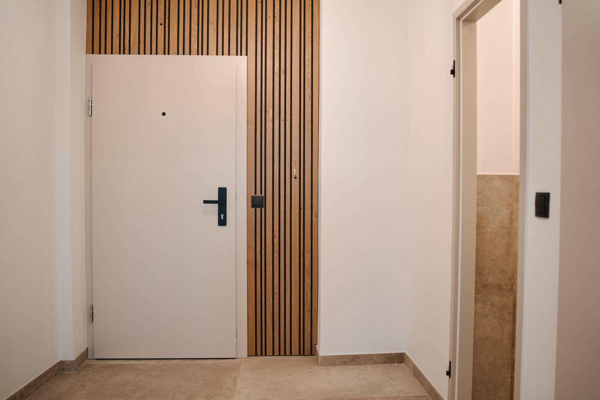 Heller Eingangsbereich mit moderner Holzwandverkleidung, weißer Tür und Fliesenboden.