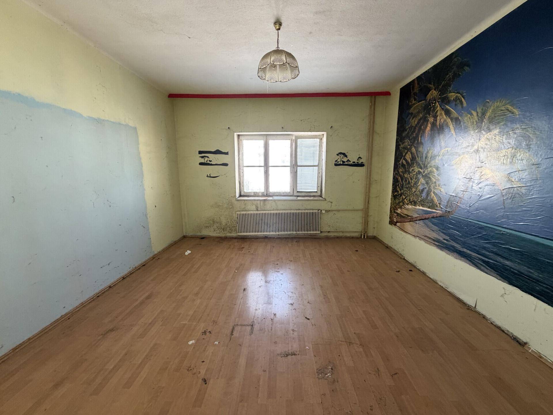 Buntes Zimmer mit Laminatboden und Wandgemälde, das eine tropische Szene darstellt.