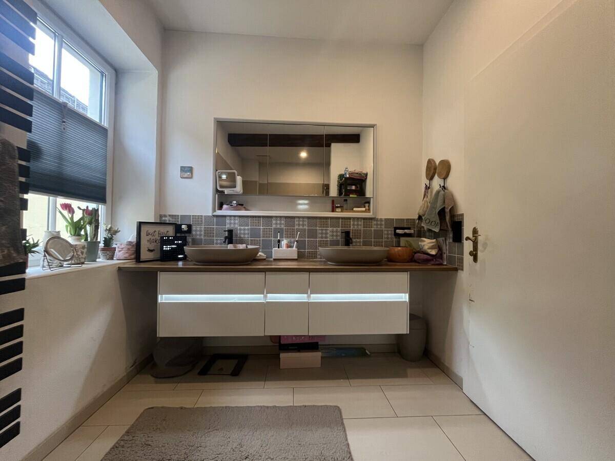 Geräumiges Badezimmer mit Doppelwaschbecken, Spiegelschrank und Fenster für Tageslicht.