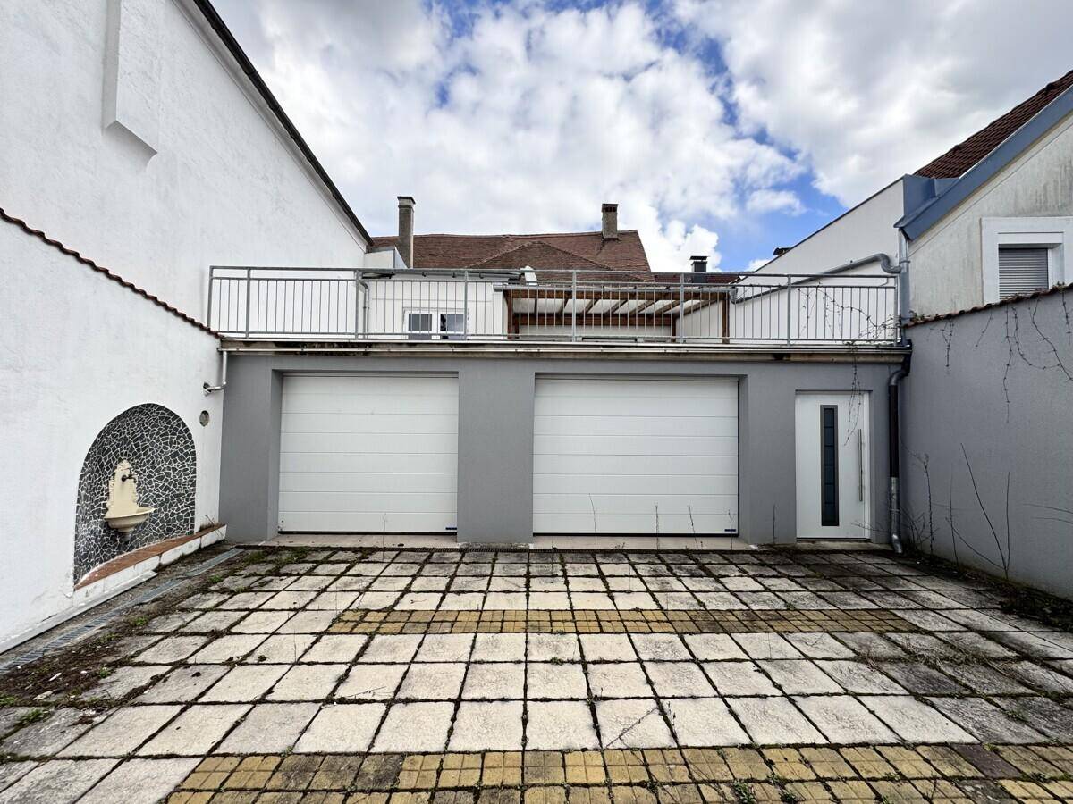 Außenansicht des Gebäudes mit zwei Garagentoren und einer gepflasterten Hoffläche.