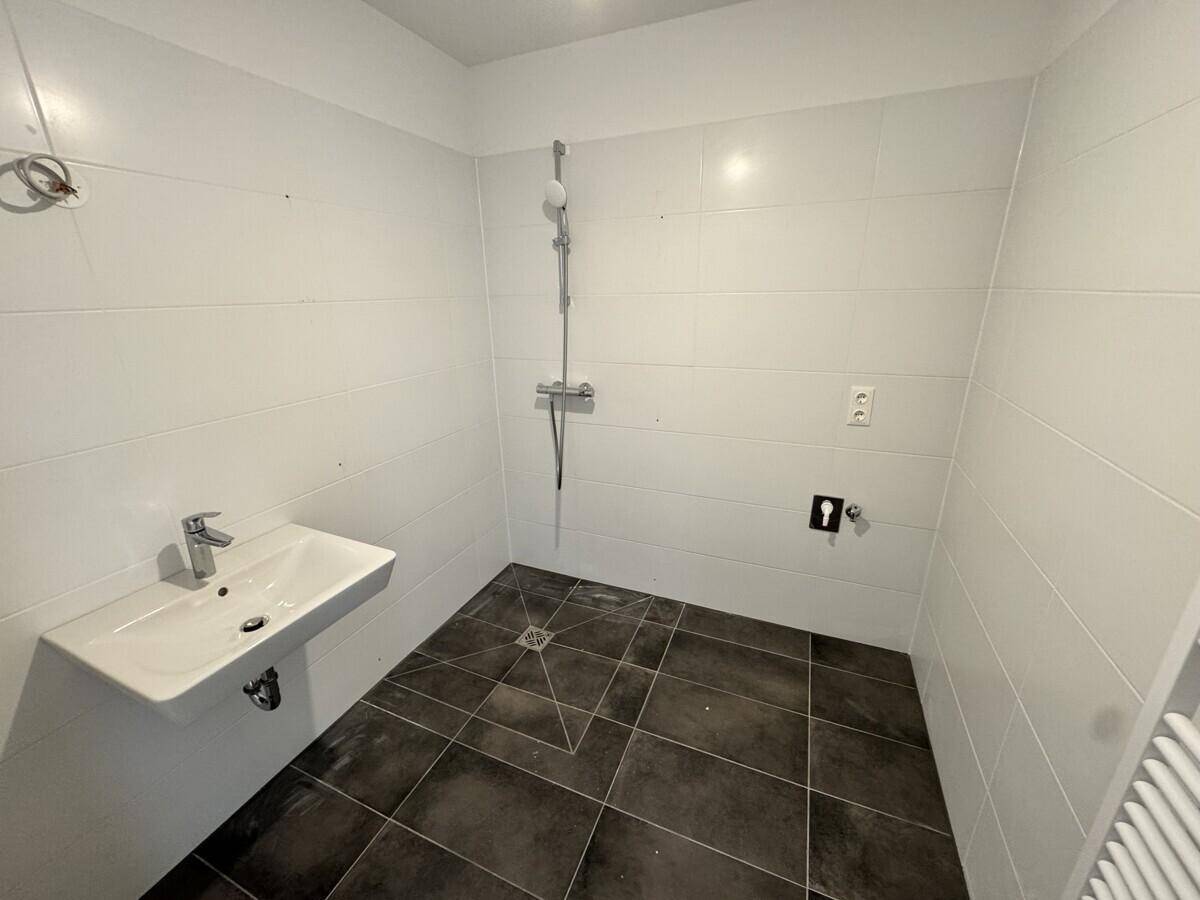 Modernes Badezimmer mit weißen Fliesen, dunklem Boden und ebenerdiger Dusche.