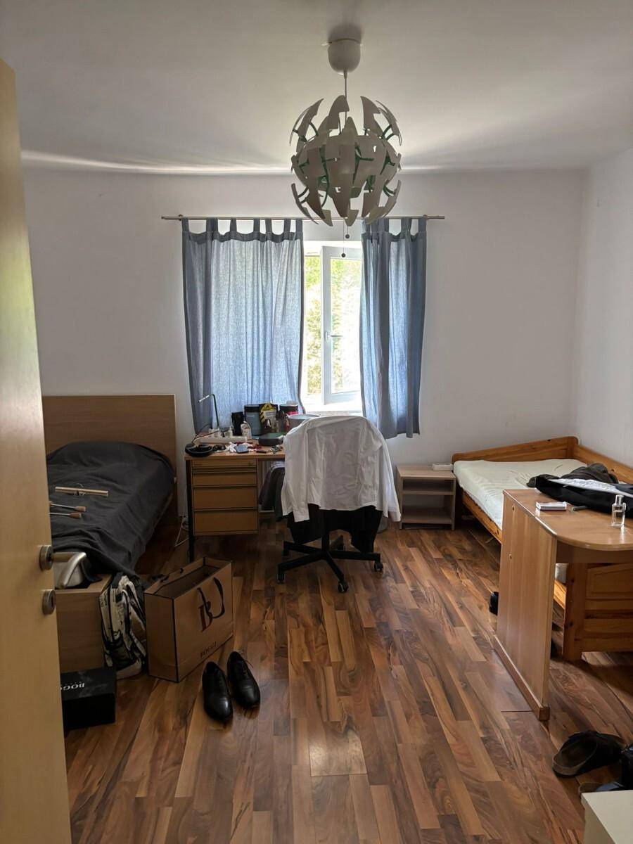 Schlafzimmer mit Bett, Schreibtisch und Fenster, das für natürliche Belichtung sorgt.