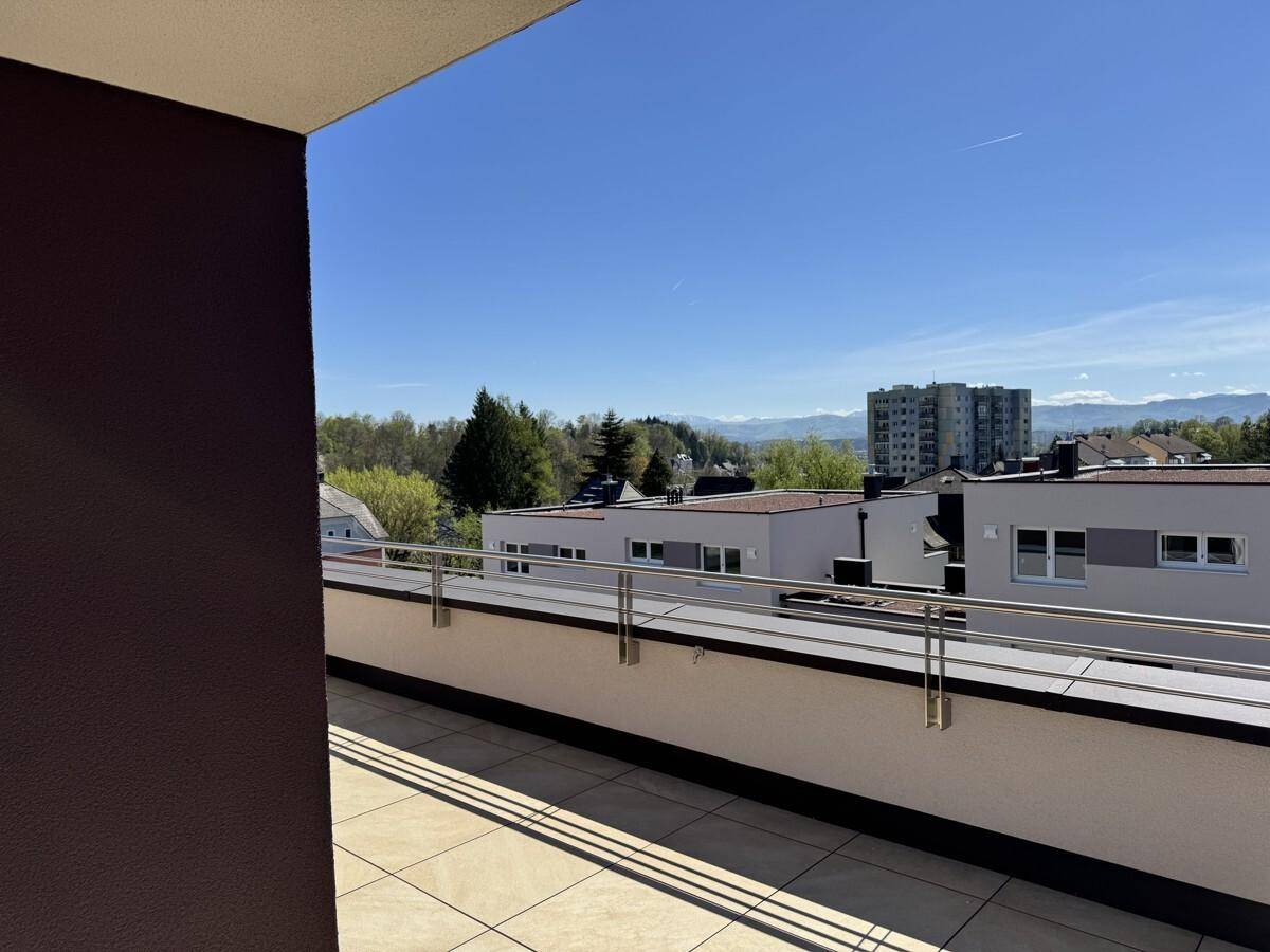 Weitläufige Terrasse mit Metallgeländer und Panoramablick auf die grüne Umgebung und Berge.