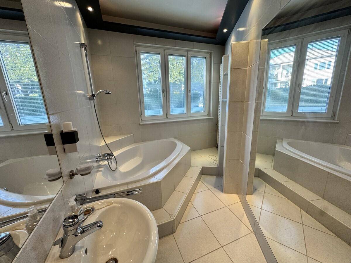 Großes Badezimmer mit Eckbadewanne, separater Dusche und mehreren Fenstern für natürliche Belüftung.