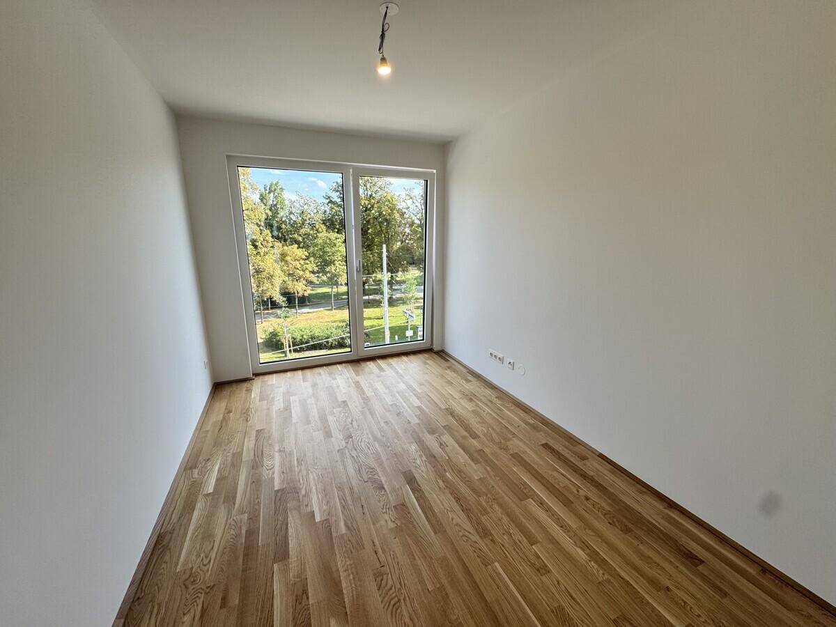 Helles Schlafzimmer mit Parkettboden und großen Fenstern, die einen Blick ins Grüne bieten.