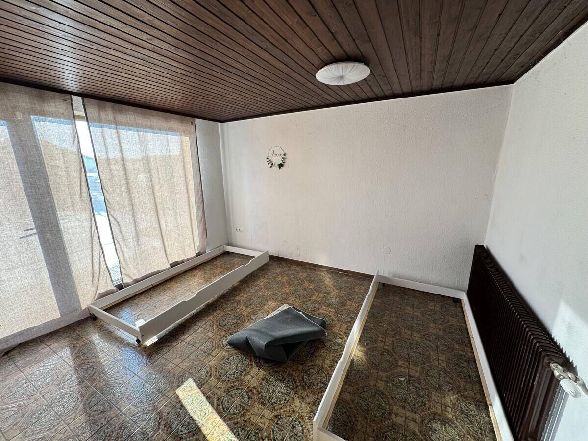 Schlafzimmer mit dunkler Holzdecke, gemustertem Boden und Zugang zum Außenbereich.