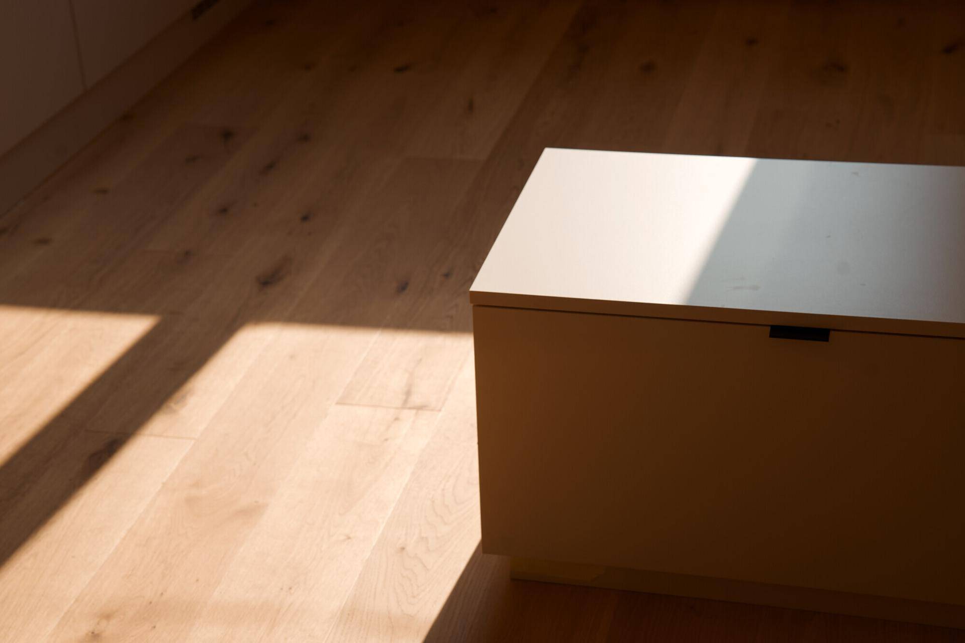 Heller Holzboden mit einem niedrigen Schrank, beleuchtet von natürlichem Sonnenlicht.