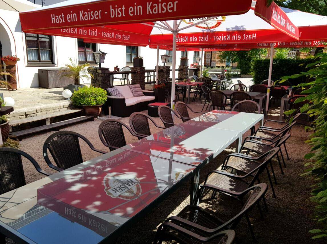 Großer Außenbereich mit zahlreichen Tischen und roten Sonnenschirmen für Gäste.