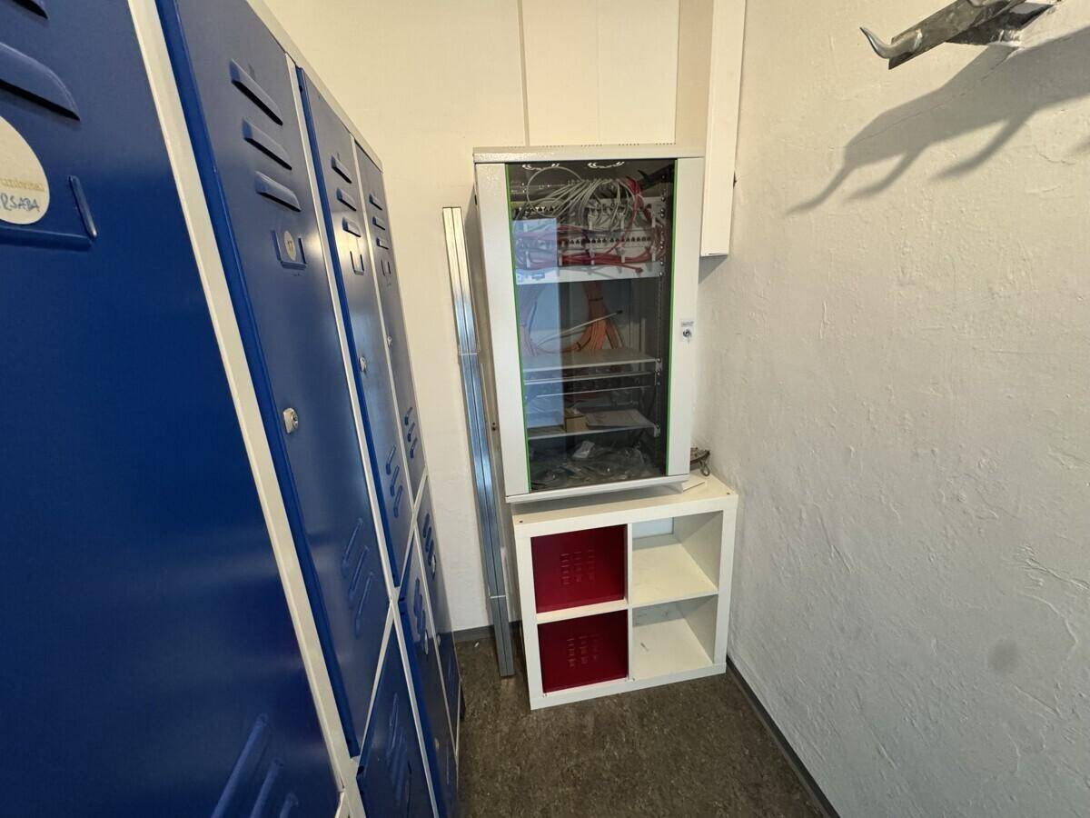 Lagerraum mit blauen Spinden und einem Serverschrank, geeignet für technische Ausstattung oder persönliche Gegenstände.