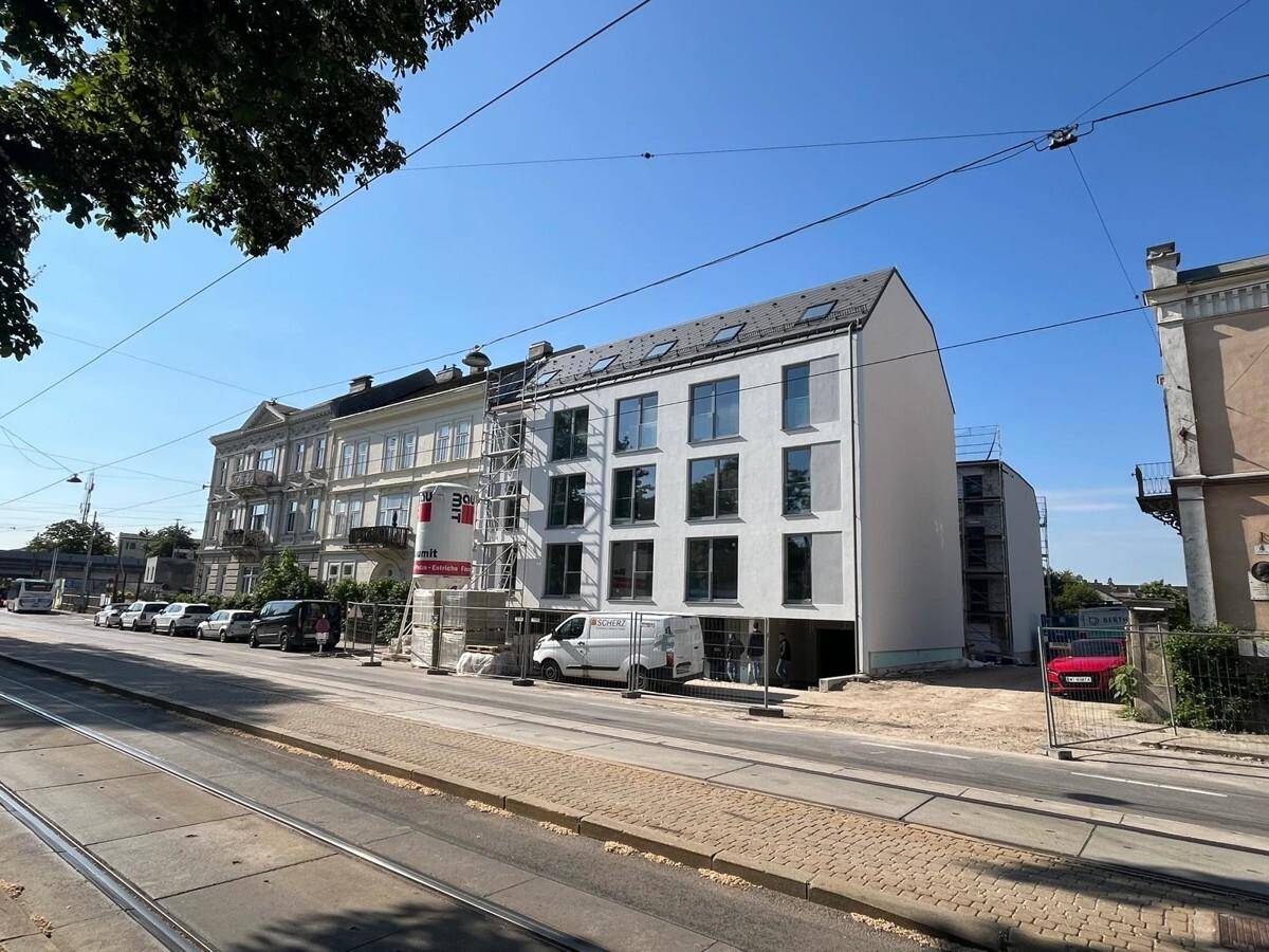 Neubau in Bauphase mit Gerüst an der Fassade, gelegen an einer Straße mit Straßenbahnschienen.