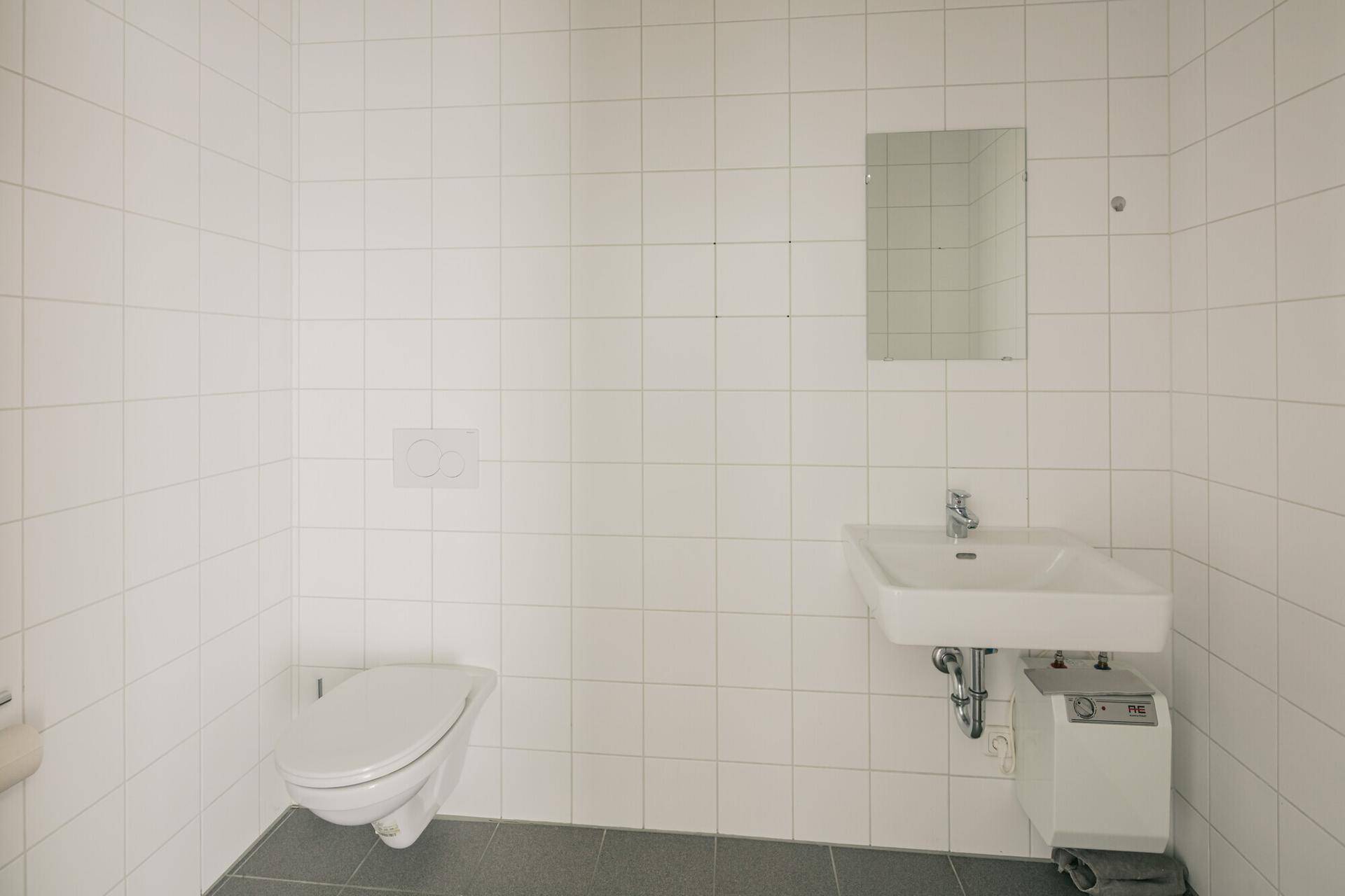 Sauberes Badezimmer mit weißen Wandfliesen, wandhängender Toilette und modernem Waschbecken.