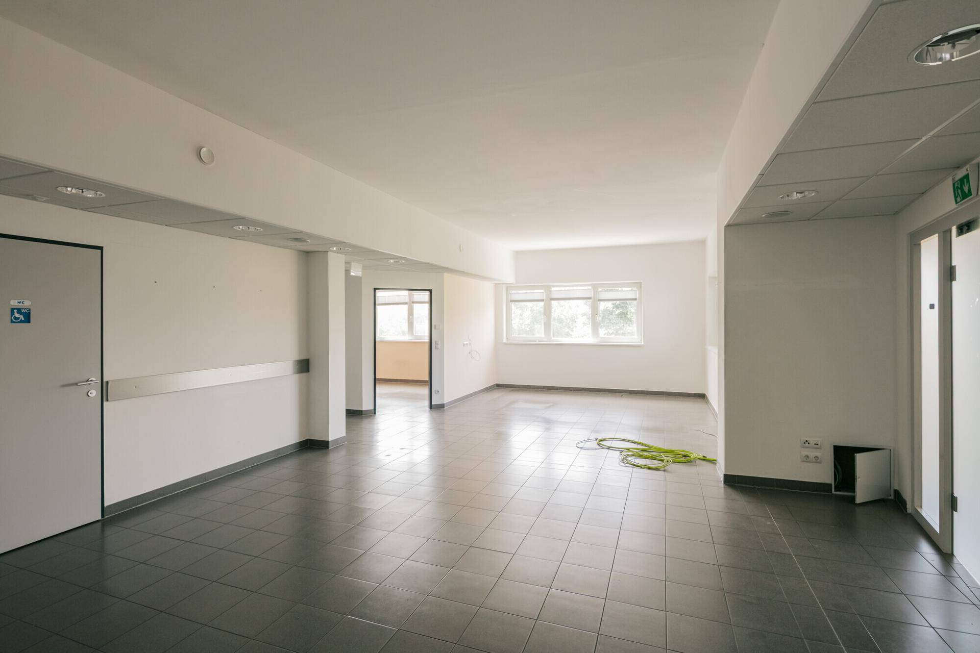 Großer, leerer Büroraum mit grauen Fliesen und abgehängter Decke, bereit zur Einrichtung.