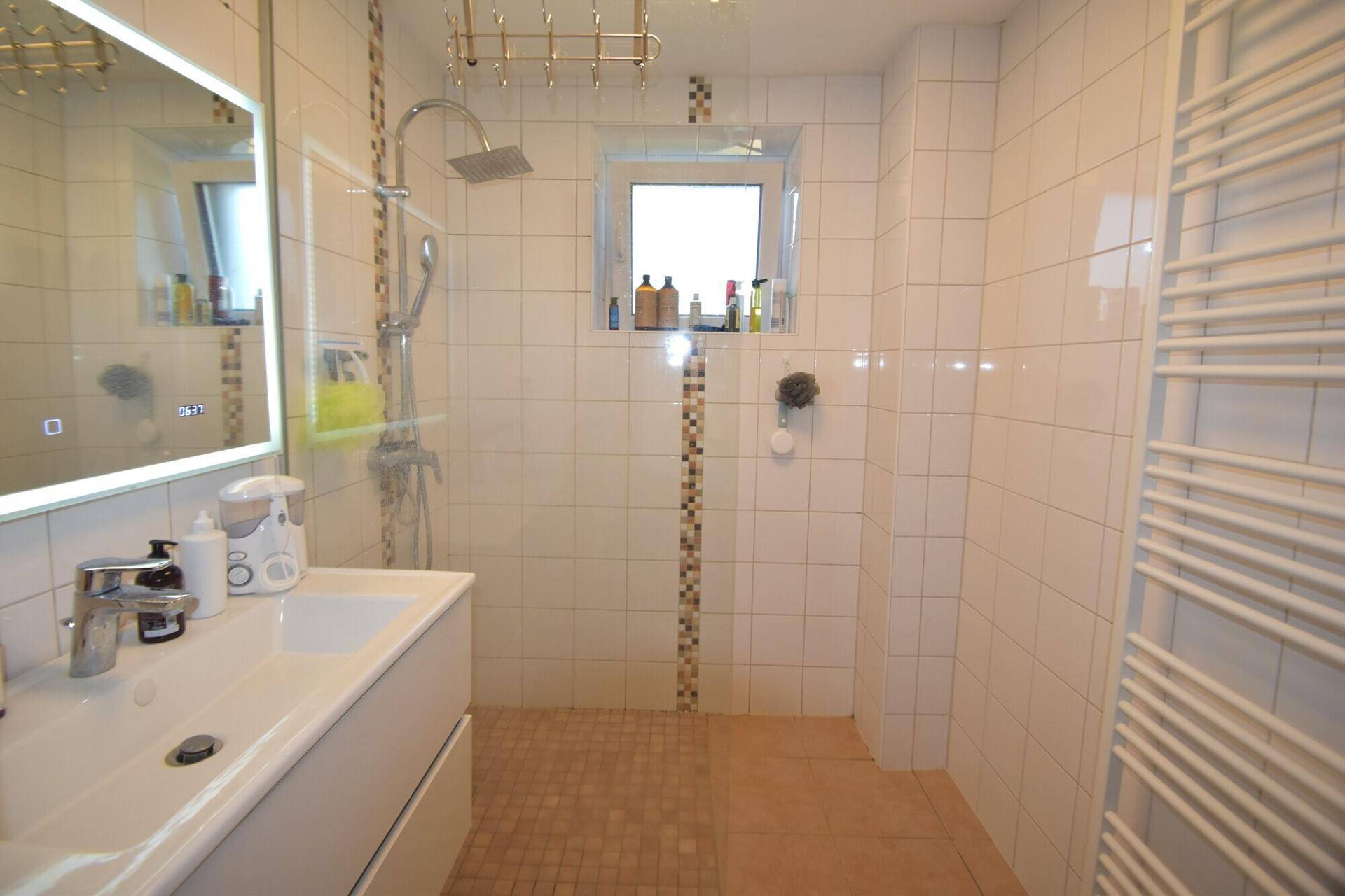 Modernes Badezimmer mit großer ebenerdiger Dusche, Fenster und Handtuchheizkörper.