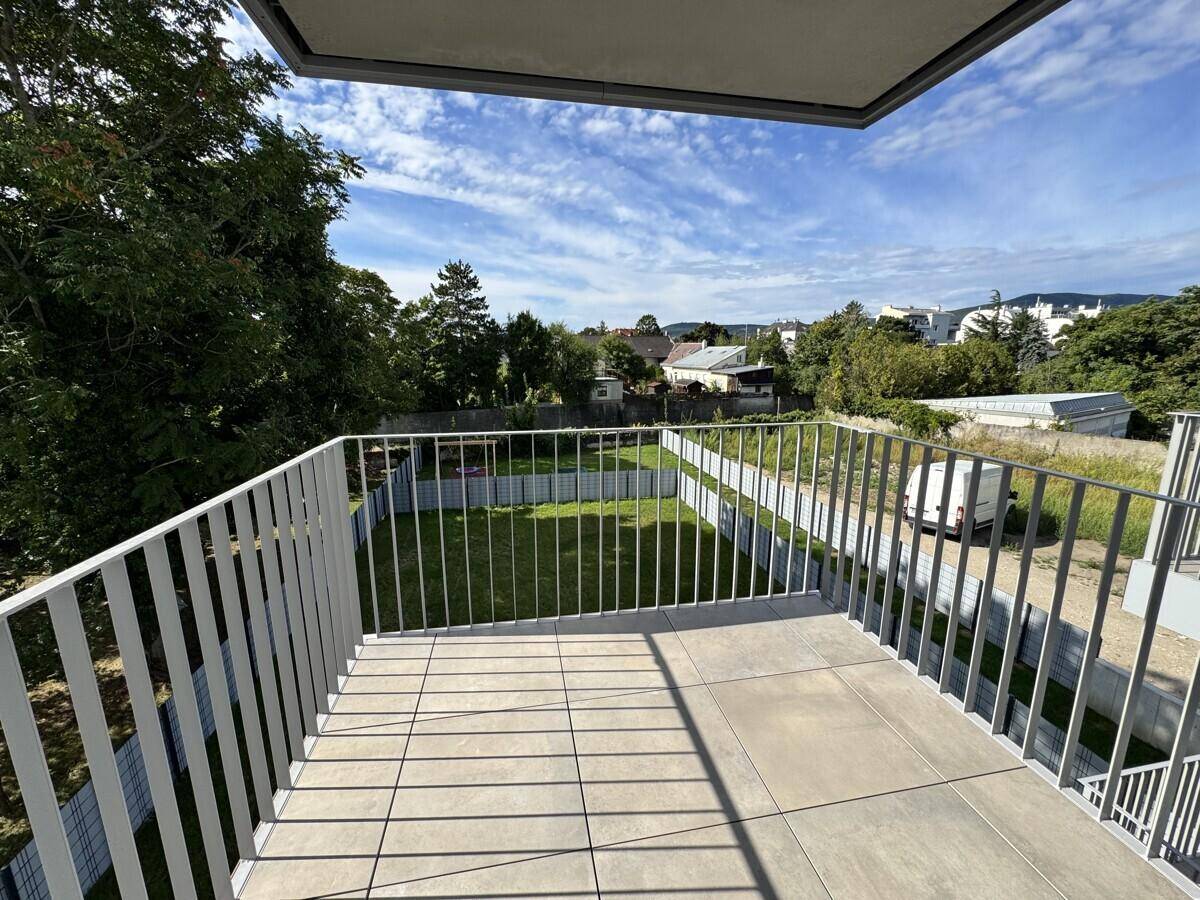 Geräumiger Balkon mit Fliesenboden und Blick auf eine grüne Wiese und Bäume.