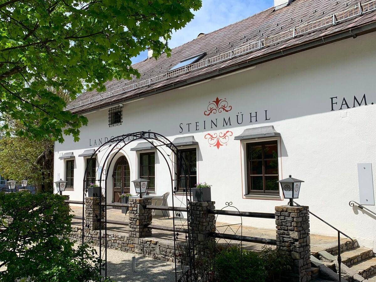 Seitenansicht des Landgasthofs Steinmühl mit traditioneller Architektur und grüner Umgebung.