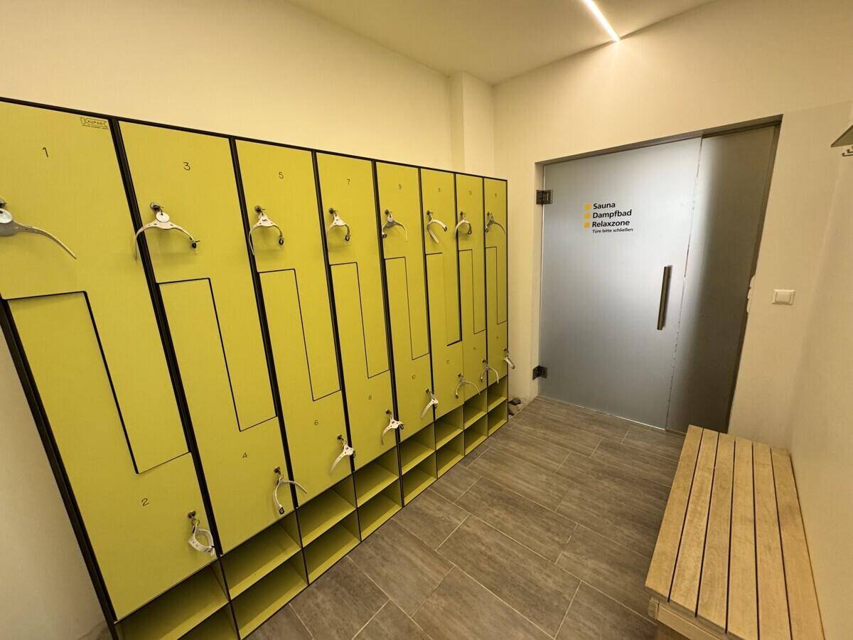 Umkleidebereich mit gelben Spinden, Sitzbank und Zugang zu Sauna und Dampfbad.