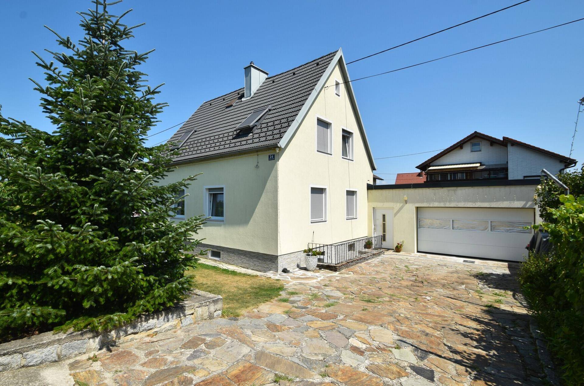 Einfamilienhaus mit heller Fassade, Satteldach und gepflasterter Auffahrt.