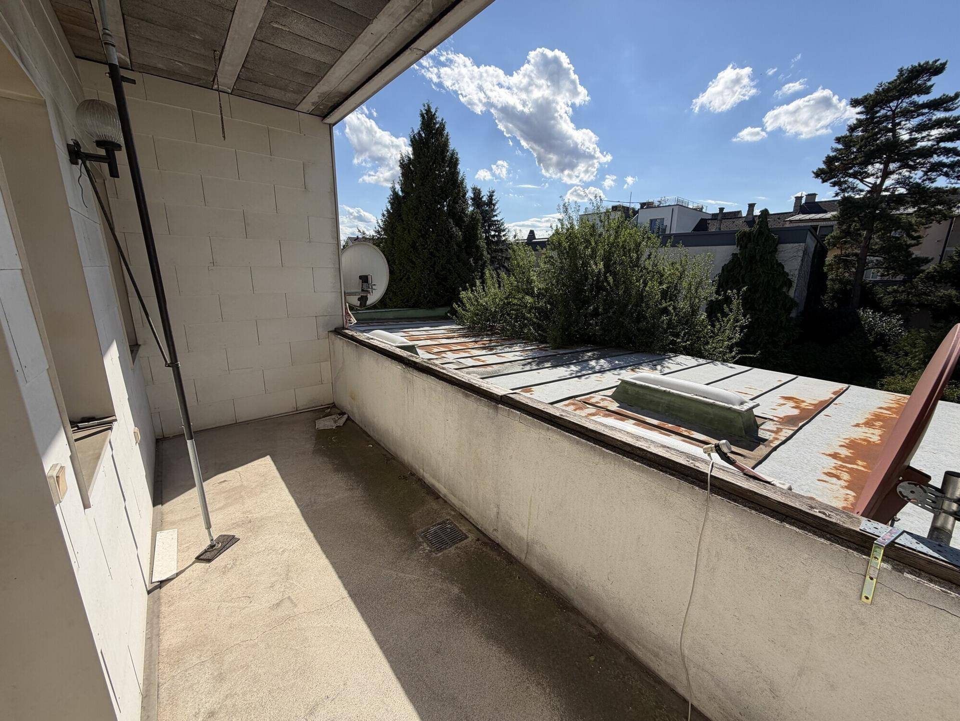 Kleiner Balkon mit Betonboden und Blick auf die umliegenden Gebäude und Bäume.