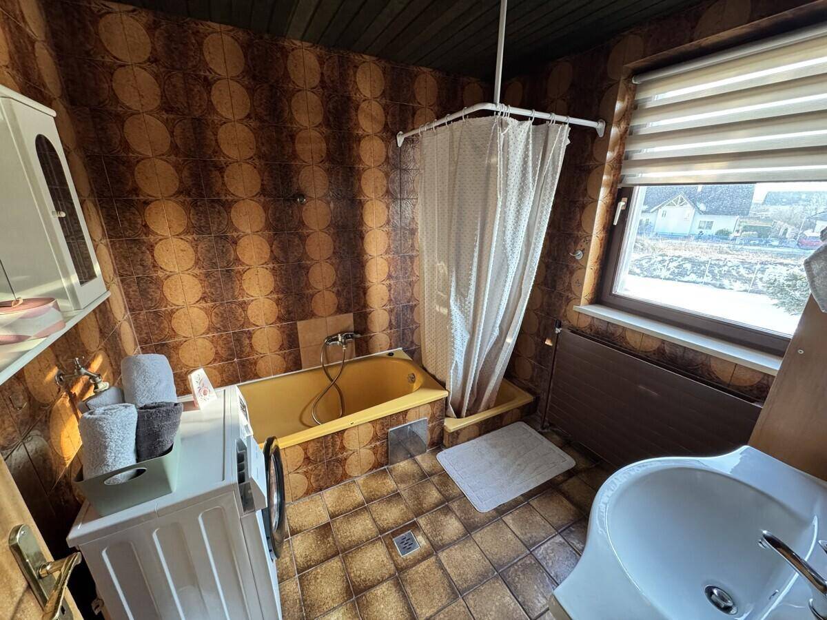 Badezimmer mit gelber Badewanne, gemusterten Fliesen und Fenster.