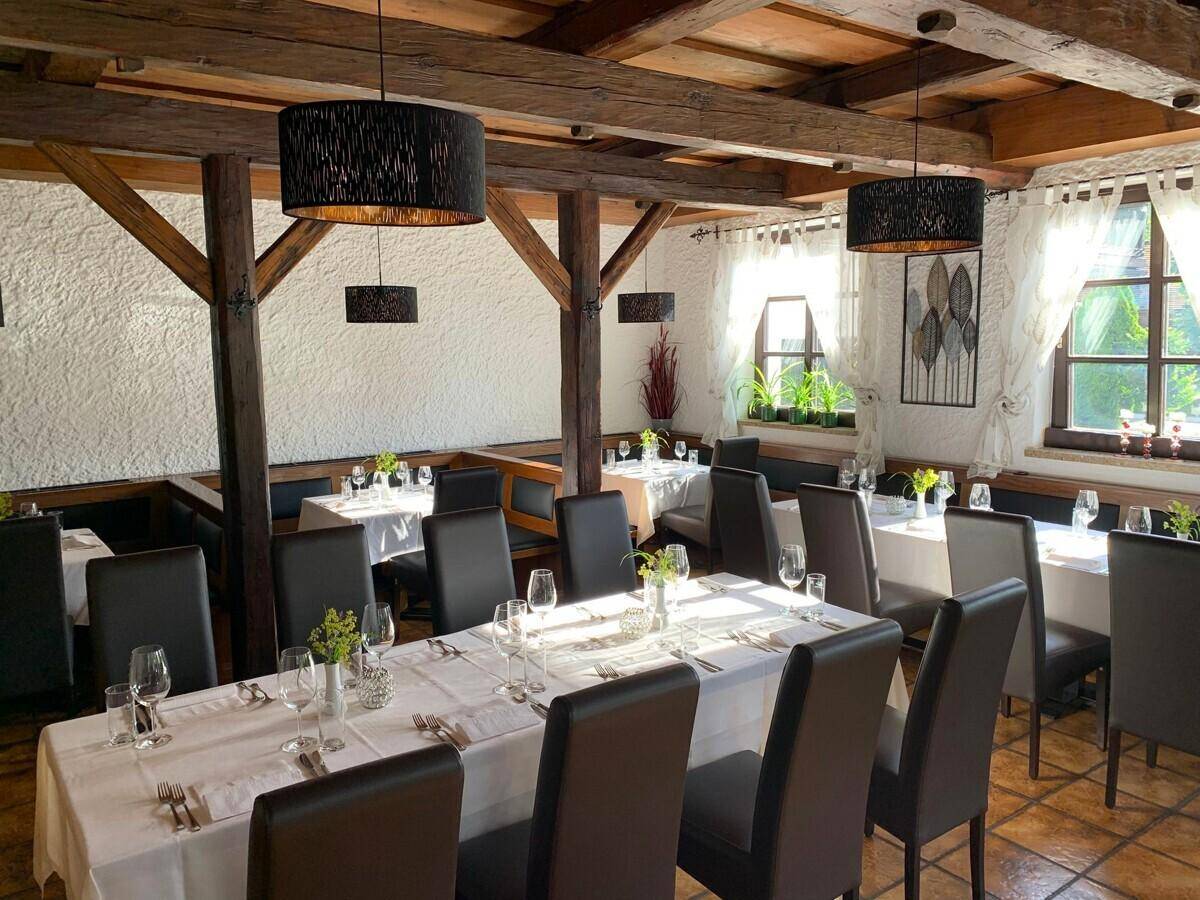 Rustikaler Speisesaal mit Holzbalken, weißen Wänden und vielen Fenstern für natürliches Licht.