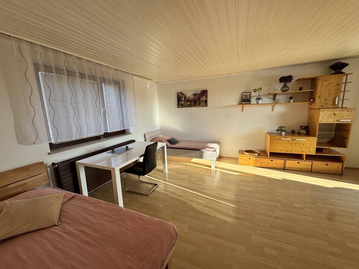 Helles Schlafzimmer mit Holzmöbeln, Laminatboden und Zugang zum Balkon.