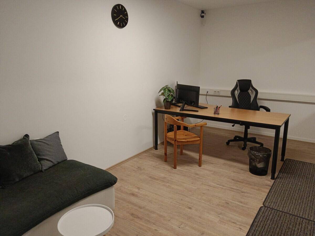 Heller Büroraum mit Schreibtisch, Sitzgelegenheit und Laminatboden.