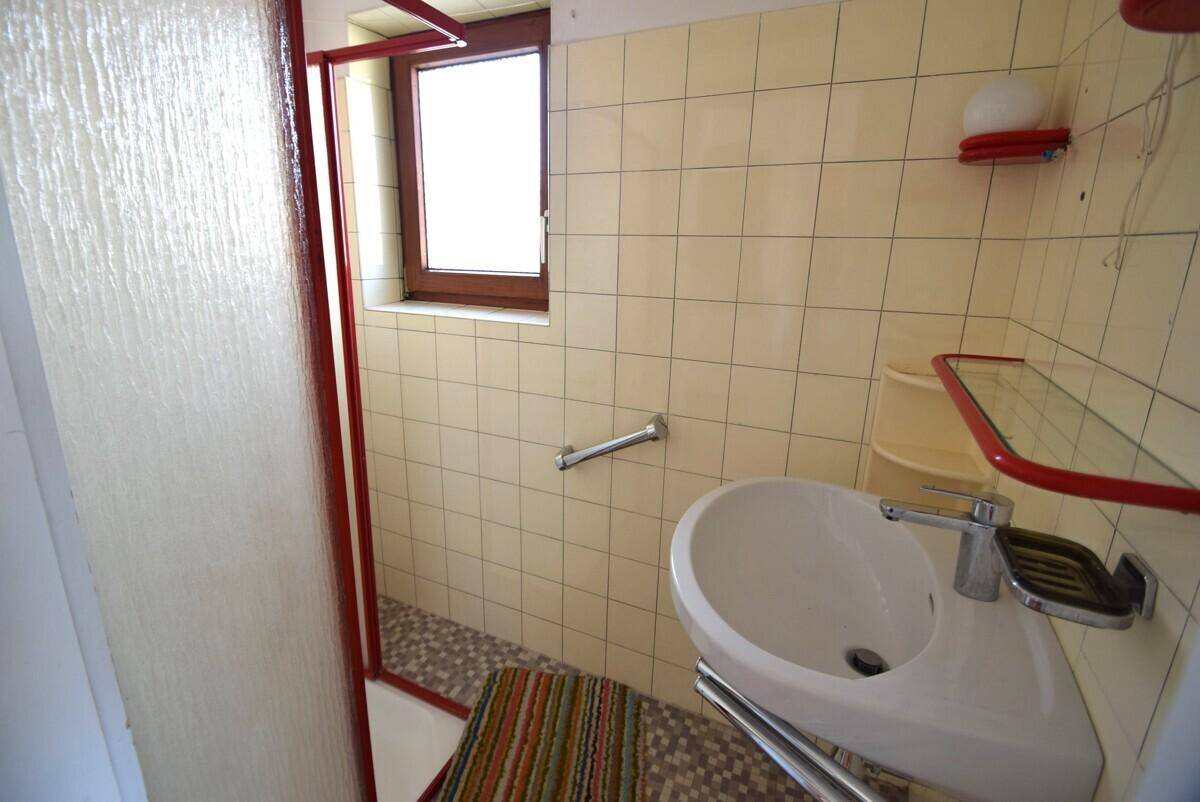 Kleines Badezimmer mit Dusche, Fenster und beigen Fliesen.