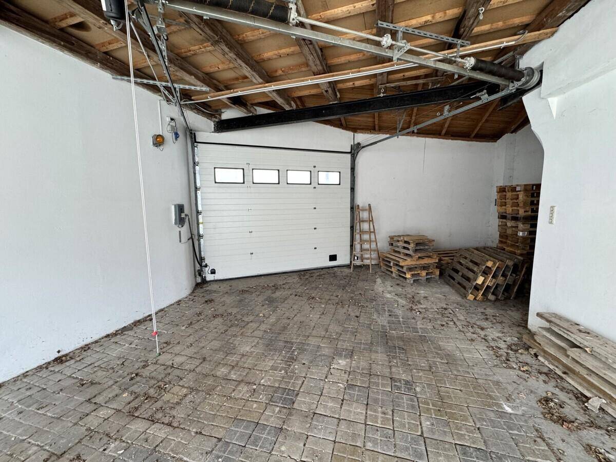 Große Garage mit Rolltor, Holzdachkonstruktion und Pflastersteinboden.