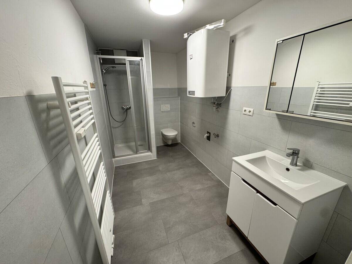 Modernes Badezimmer mit Dusche, WC, Waschbecken und beheiztem Handtuchhalter.