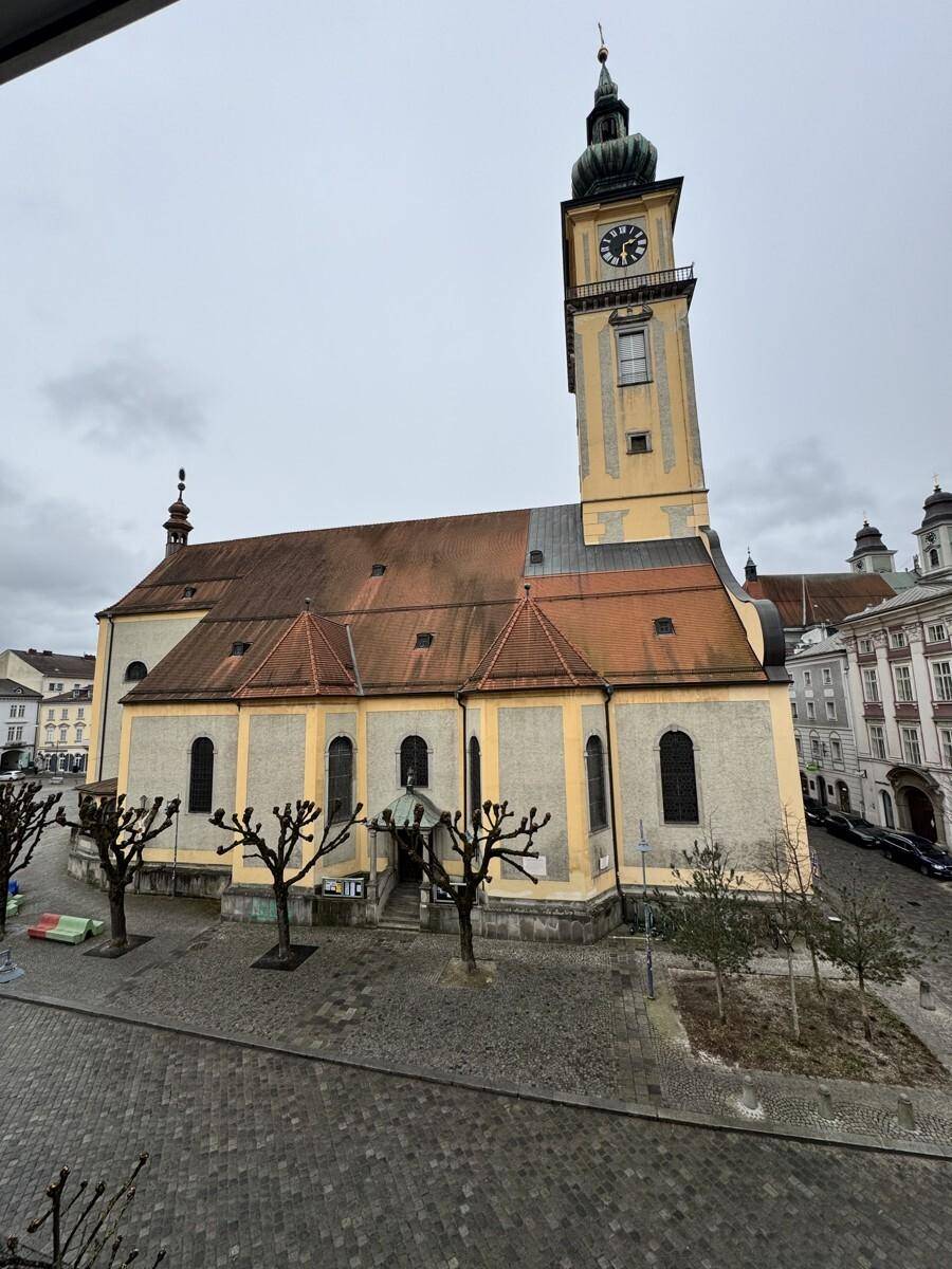 Blick auf eine historische Kirche mit Turm und Uhr, umgeben von einem gepflasterten Platz.