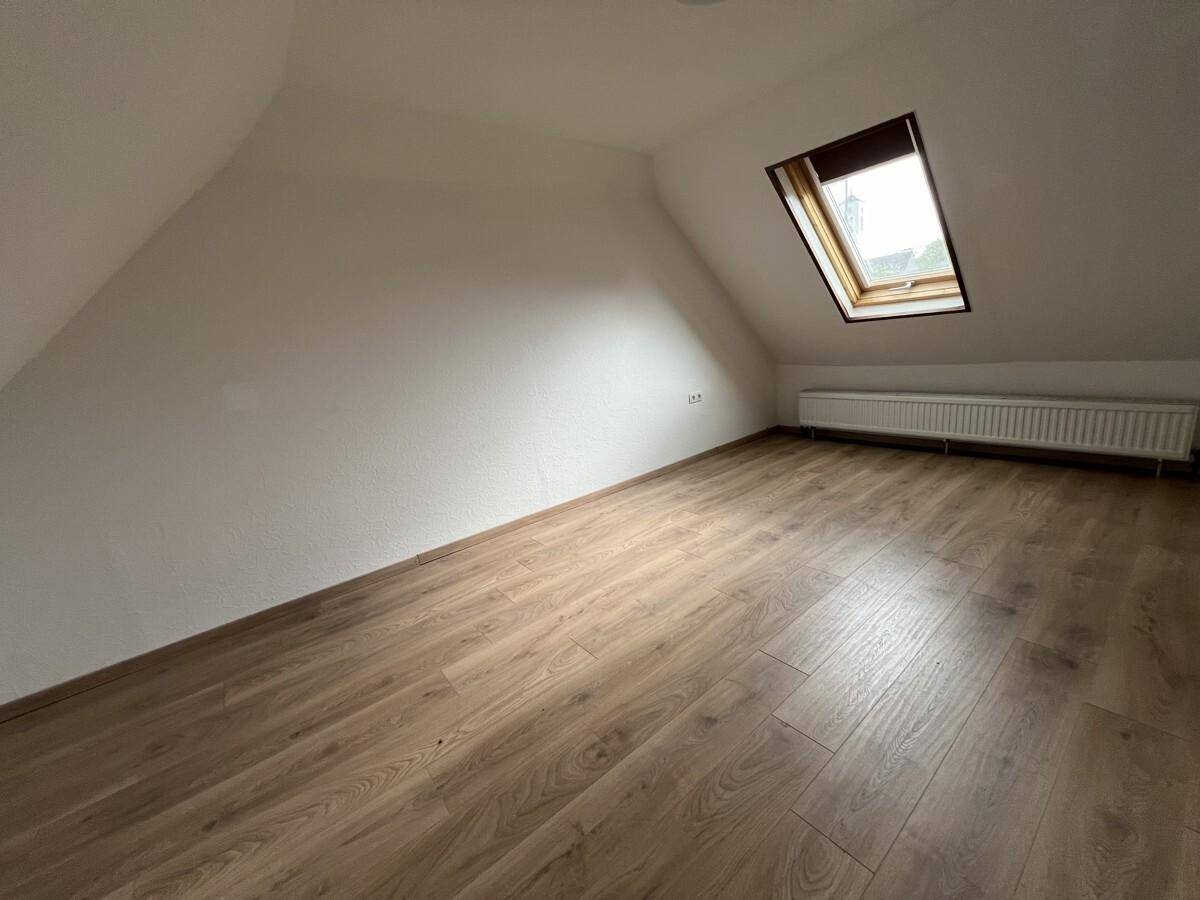 Helles Dachzimmer mit Laminatboden, schrägen Wänden und Dachfenster.