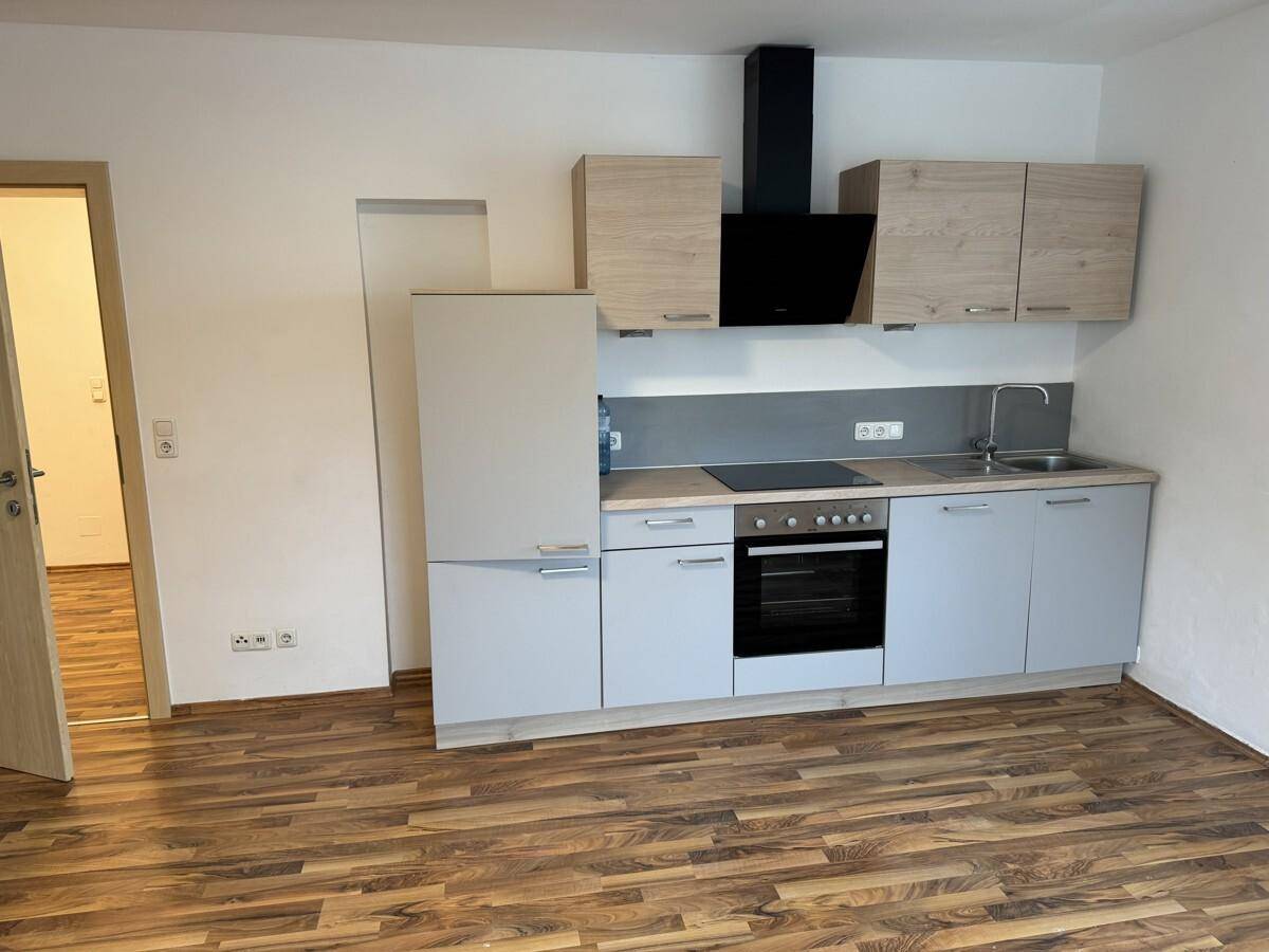 Kompakte Einbauküche mit hellgrauen Fronten, Holzoptik-Arbeitsplatte und integrierten Geräten.