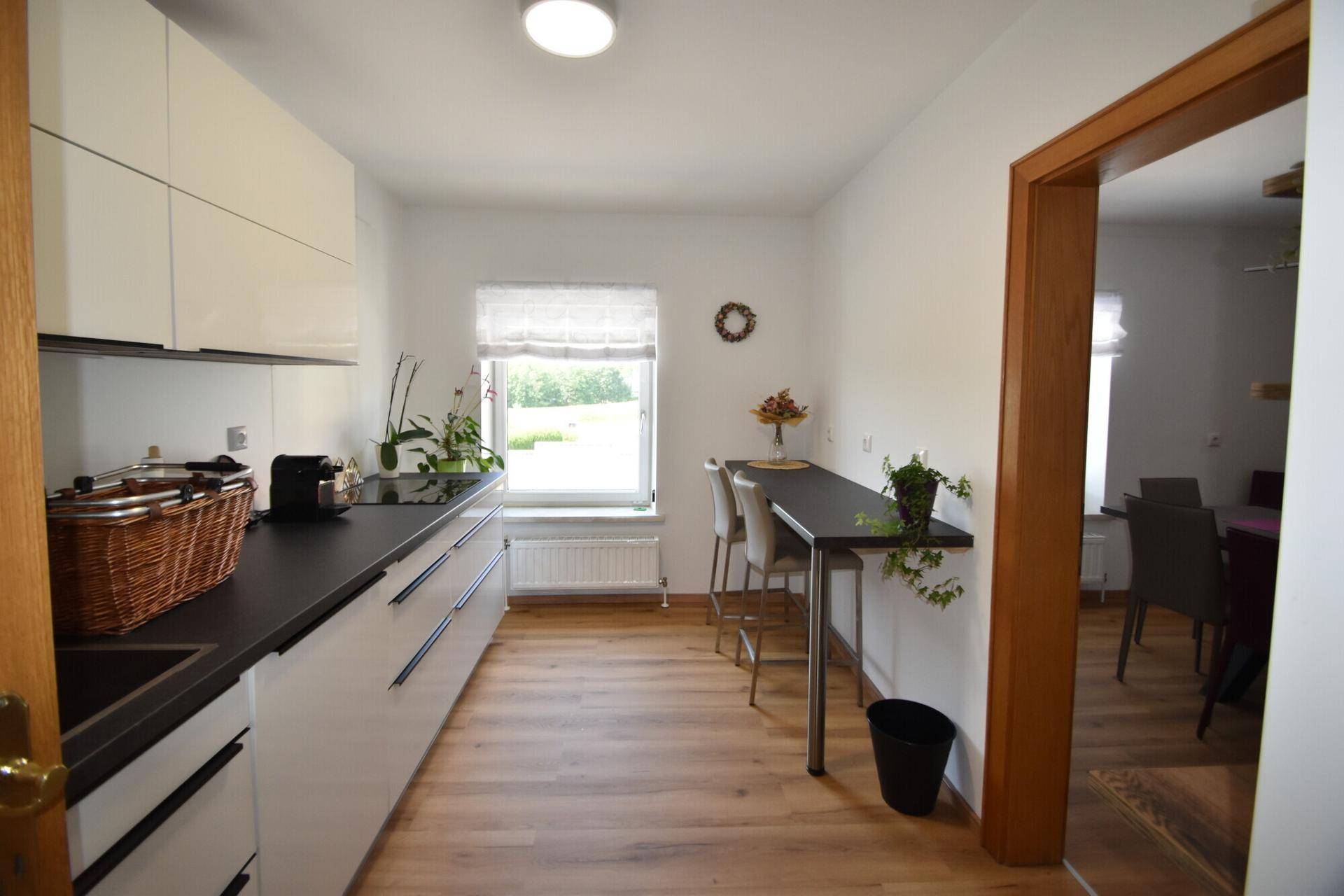 Moderne Küche mit weißen Schränken, dunkler Arbeitsplatte und Frühstücksbar mit Blick ins Grüne.