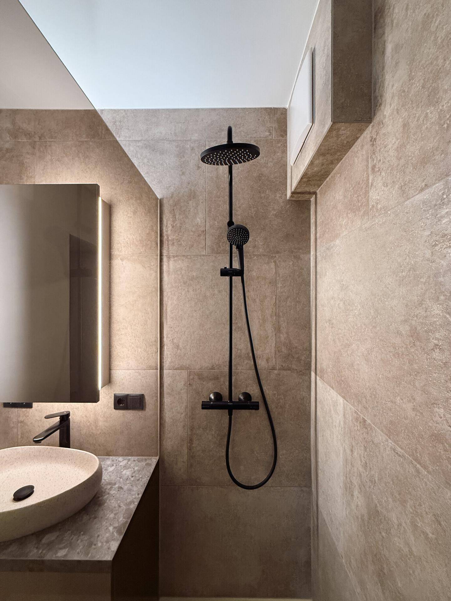 Detailansicht der modernen Dusche mit schwarzem Regenduschkopf und beigefarbenen Wandfliesen.