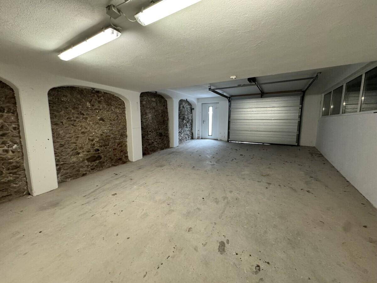 Geräumige Garage mit Betonboden, Rolltor und freigelegten Steinwänden.