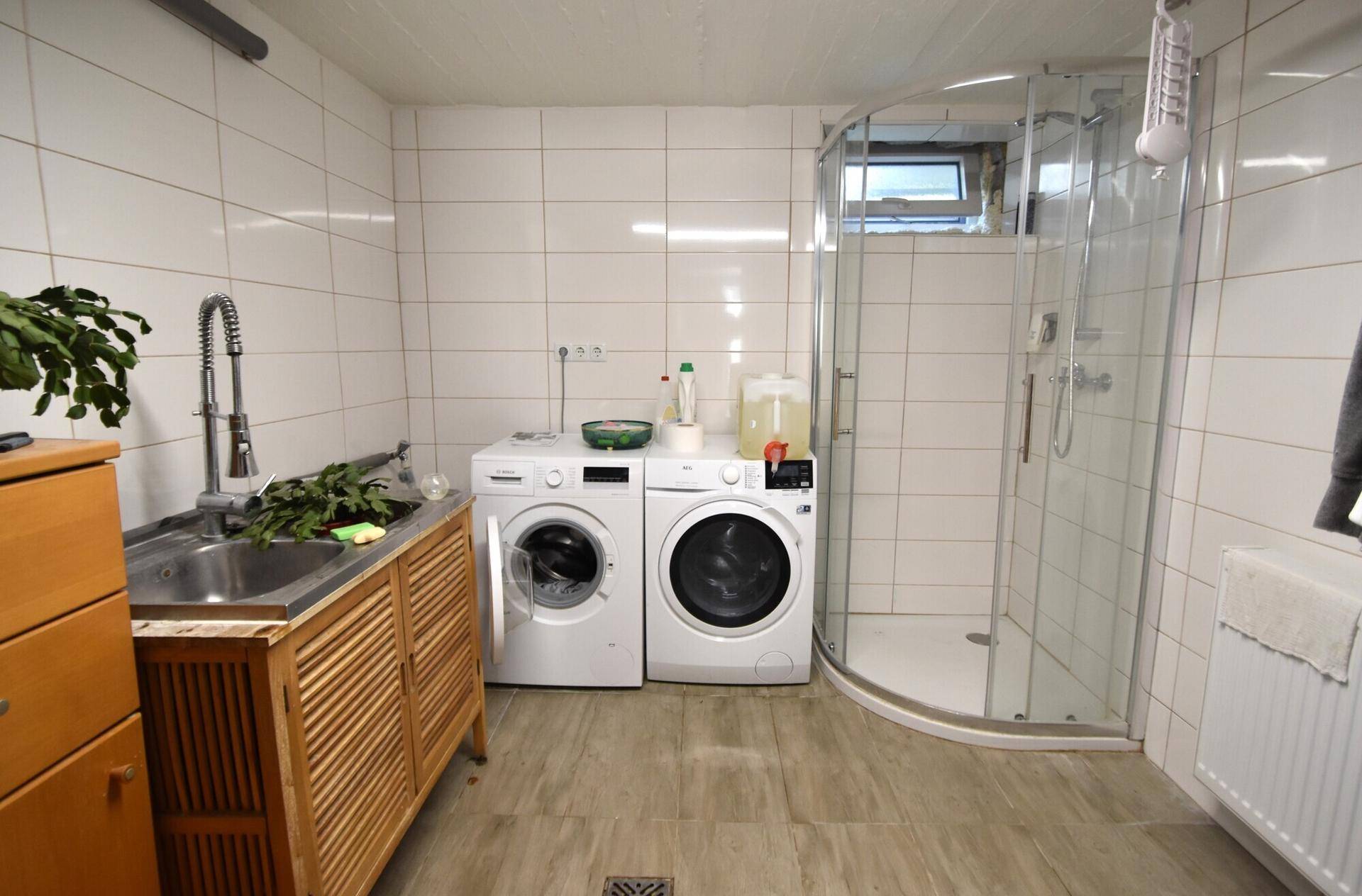 Waschküche mit Waschmaschine, Trockner, Spülbecken und Duschkabine.