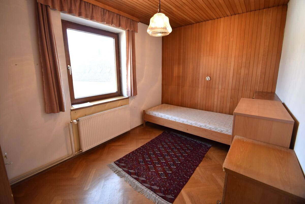 Schlafzimmer mit Holzparkett, Holzvertäfelung und einfacher Einrichtung.