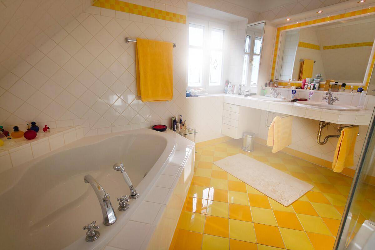 Badezimmer im 80er-Jahre-Stil mit gelben Fliesen, Eckbadewanne und Doppelwaschbecken.