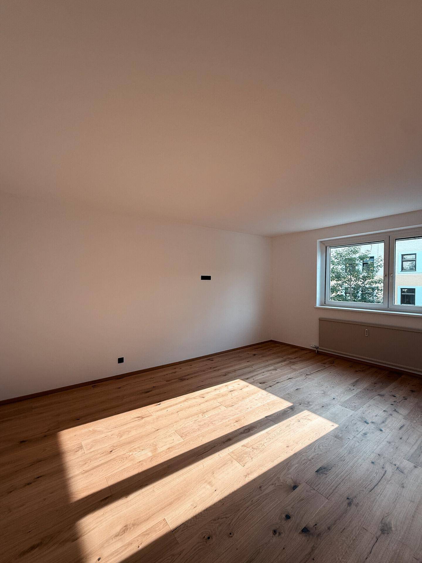 Helles Schlafzimmer mit Holzboden, weißen Wänden und Fenster mit Blick ins Grüne.