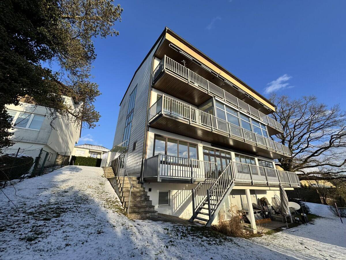 Modernes Mehrfamilienhaus mit mehreren Balkonen und großen Fenstern, umgeben von Schnee.