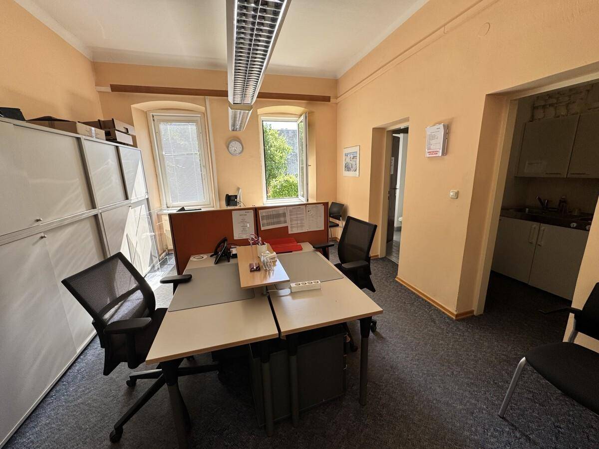 Helles Büro mit mehreren Arbeitsplätzen, Teppichboden und Fenstern mit Blick ins Grüne.