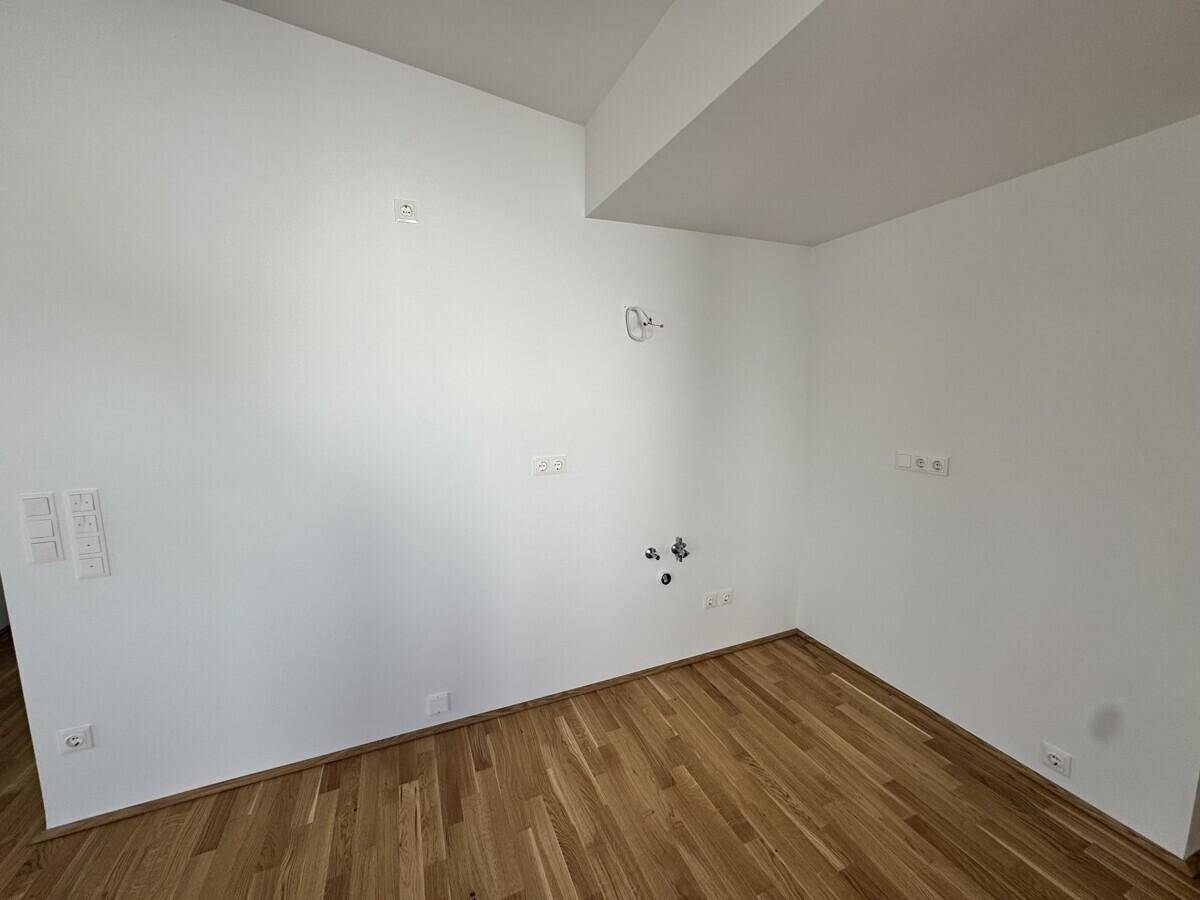 Leerer Küchenbereich mit Anschlüssen für Geräte und hellem Holzboden.
