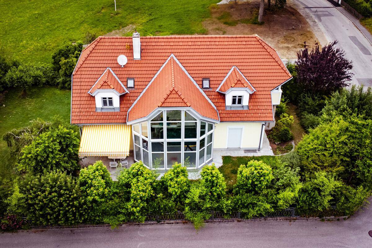 Vorderansicht des Hauses mit Wintergarten, Markise und rotem Ziegeldach, umgeben von Hecken.
