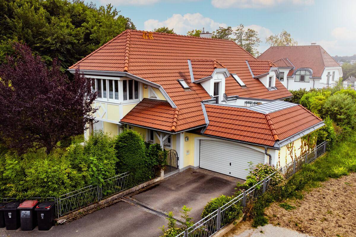 Ansicht des Hauses mit Garage, rotem Ziegeldach und gepflegter Auffahrt umgeben von Bäumen.