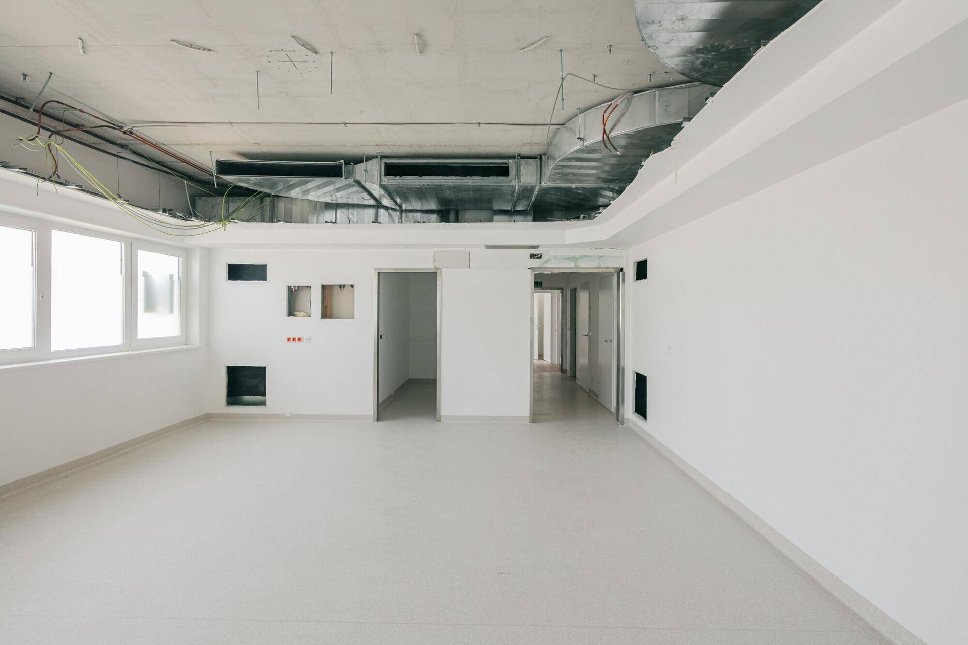Großer, heller Gewerberaum mit Vinylboden und sichtbaren Deckeninstallationen, bereit für den Ausbau.