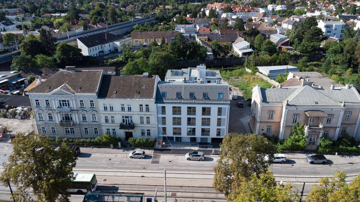 Luftaufnahme einer Straße mit verschiedenen Gebäuden, darunter ein moderner Neubau und Altbauten.