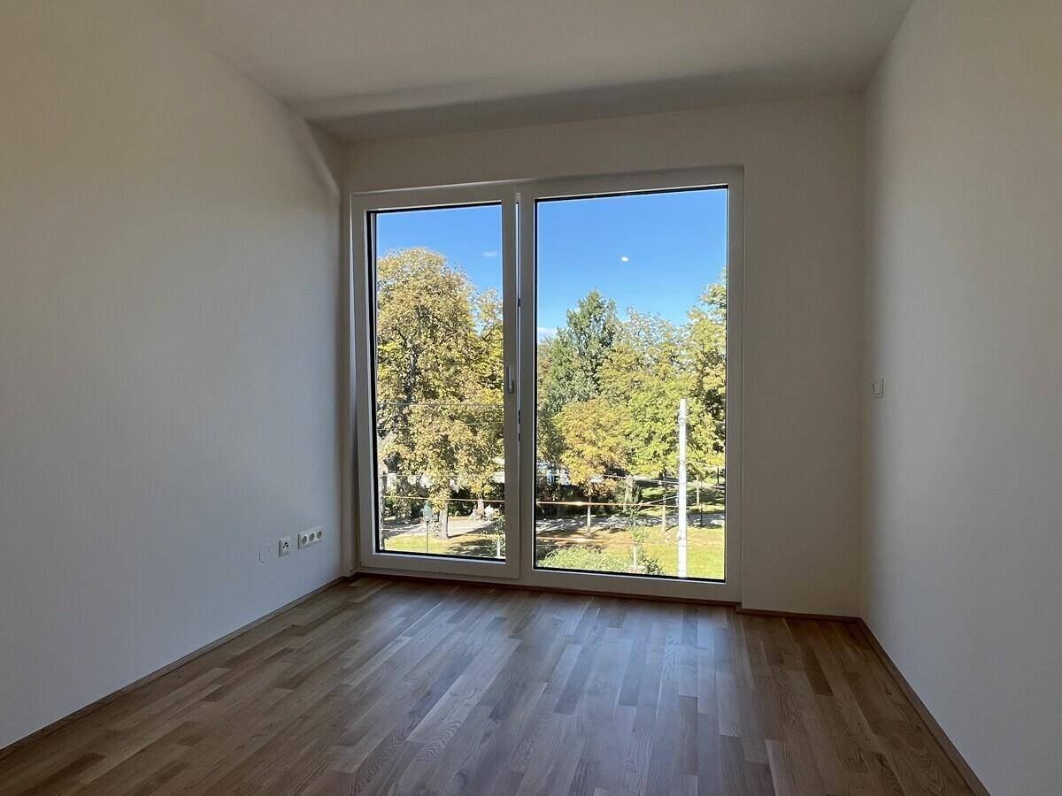 Lichtdurchflutetes Zimmer mit Holzboden und Blick ins Grüne, ideal als Schlaf- oder Arbeitszimmer.